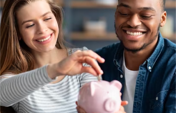 Happy couple putting a coin into their pink piggy bank