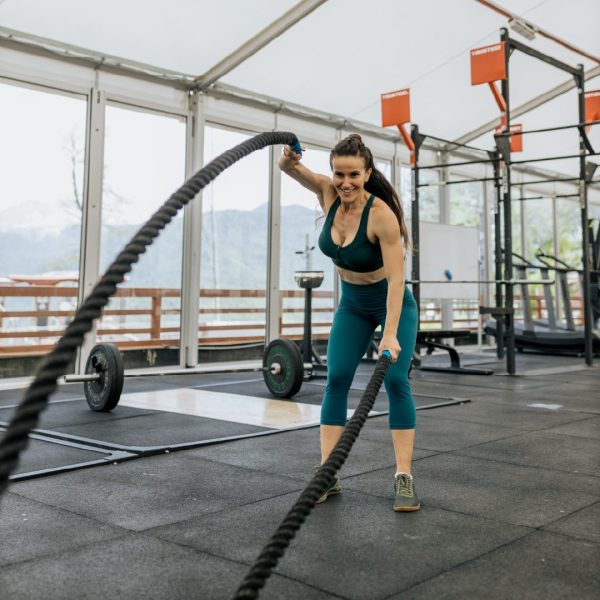 Woman swinging ropes during crossfit in gym surrounded by weights and exercise equipment