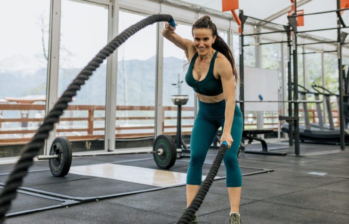Woman swinging ropes during crossfit in gym surrounded by weights and exercise equipment