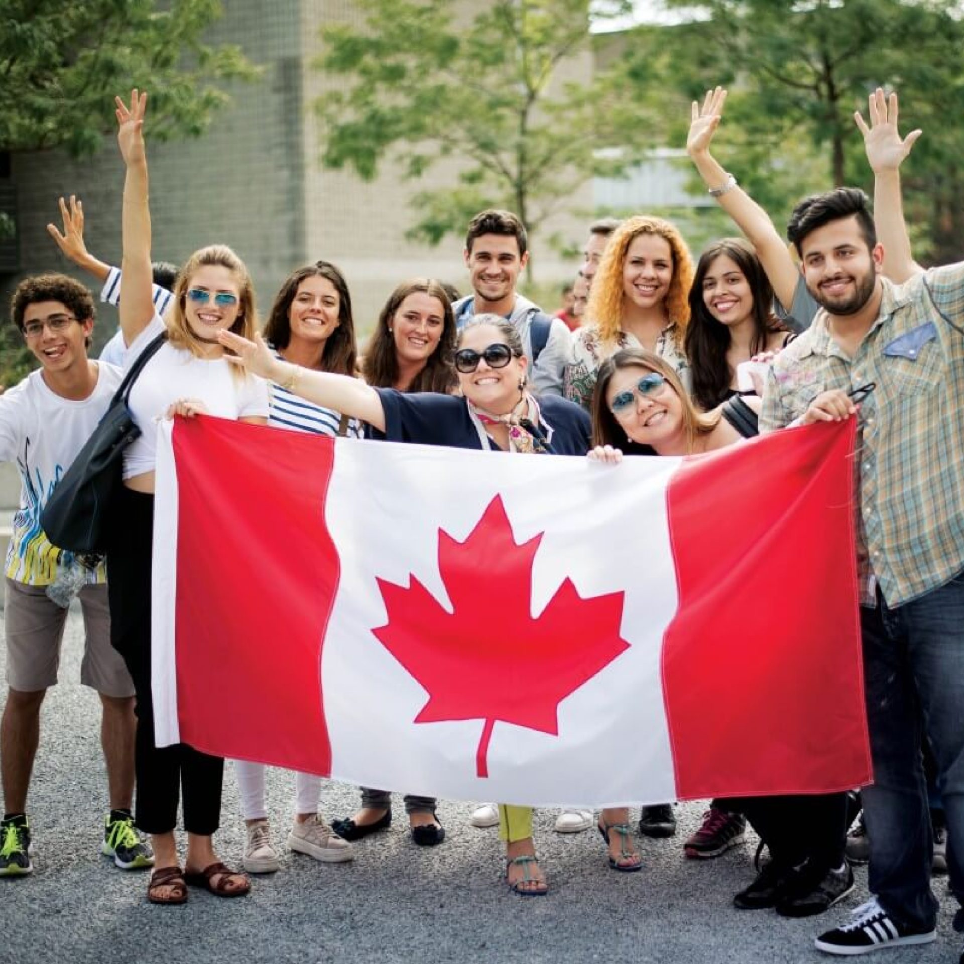 a group of people standing behind a Canadian maple leaf flag, all recent Canadian immigrants