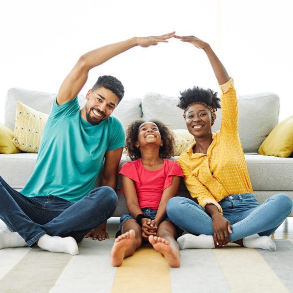 family sitting on the floor of their living room, the parents having their arms over their child who is looking up, as if to represent the protection of permanent life insurance
